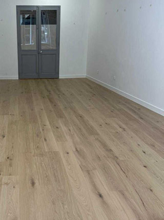 Vue d'une pièce spacieuse avec un parquet en chêne clair, des murs blancs et une double porte vitrée de couleur grise au fond, posé par la Menuiserie Jollivet à La Rochelle.