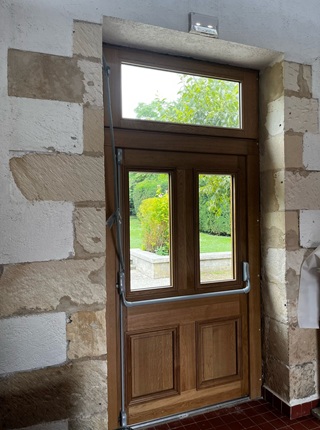 Vue intérieur d’un porte en bois avec vitrage et imposte vitrée sur crémone avec une barre anti panique