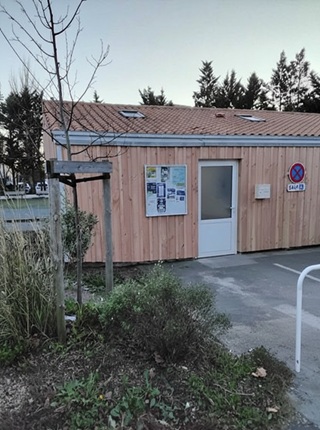 Vue de biais du local technique, mettant en valeur l’espace de verdure situé devant la porte d’accès.